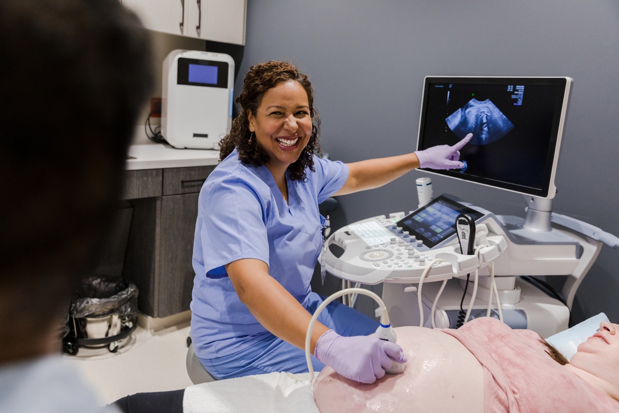 Female technician points to image on ultrasound monitor and smiles stock photo